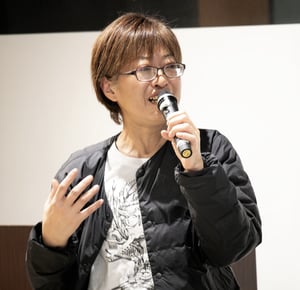 画像 シネマチュプキタバタのロゴが入った白いTシャツで、微笑みながらマイクを持つ平塚さん。 画像終わり