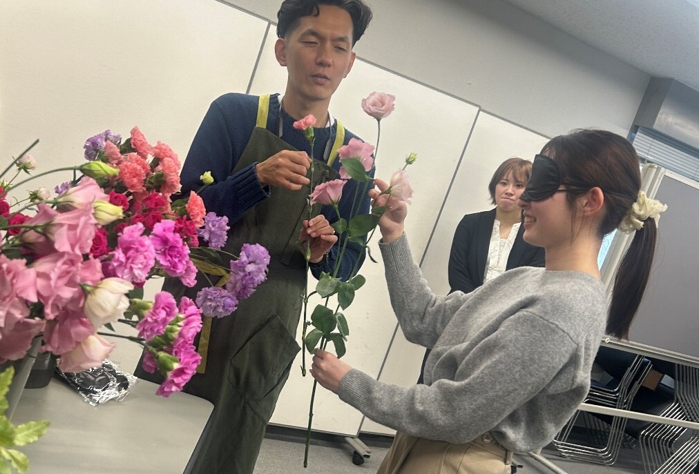 写真:イベントのリハーサル風景。目隠しをしている中野さんにお花を差し出す石井さん