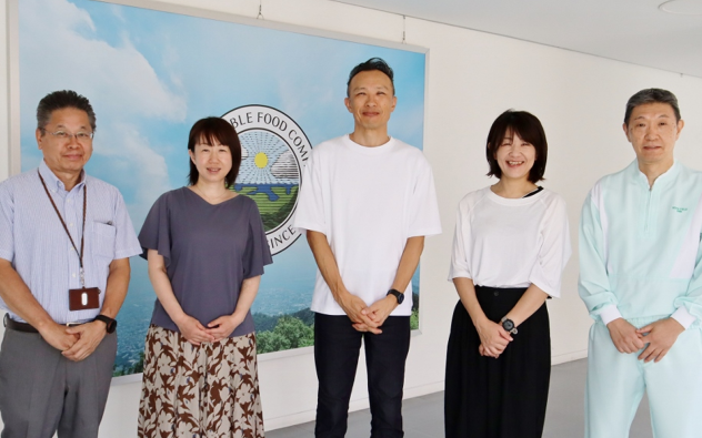 画像:『しずかでうるさい洋食屋さん』で食品を提供してくださる株式会社ロック・フィールド冷凍食品推進室の皆さん。写真中央で、メンバーの皆さんに囲まれ、白いTシャツで微笑むのが、今回インタビューさせていただいた田中さん。画像終わり