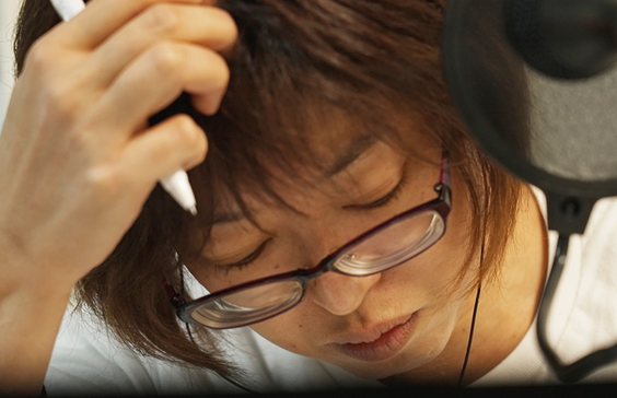 画像：心の通訳者たちの劇中写真。平塚さんがペンを片手に、悩むように目を伏せている。画像終わり