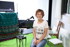 画像：シネマ・チュプキ・タバタ代表の平塚さんの写真。音声ガイドで使用するマイクの前でほほ笑んでいる。画像終わり